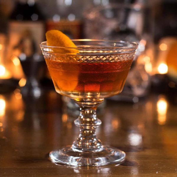 A cocktail in a vintage coupe glass with an orange peel garnich