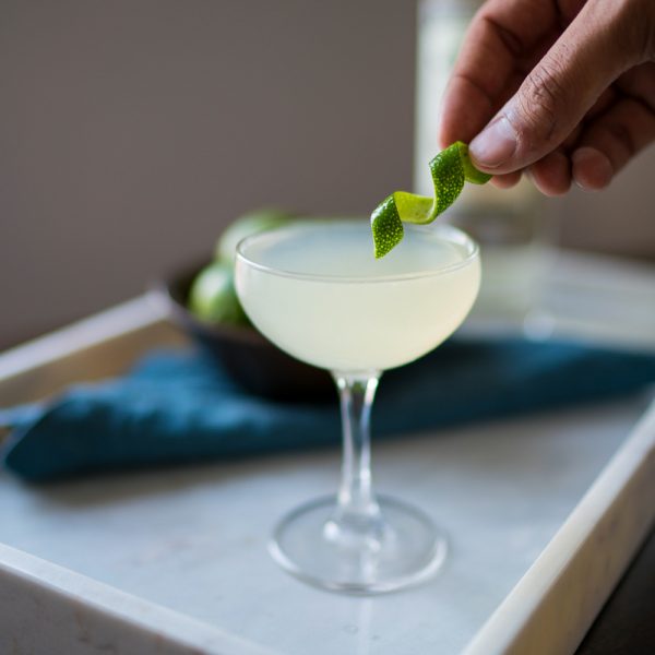 A hand placing a lime twist into a martini