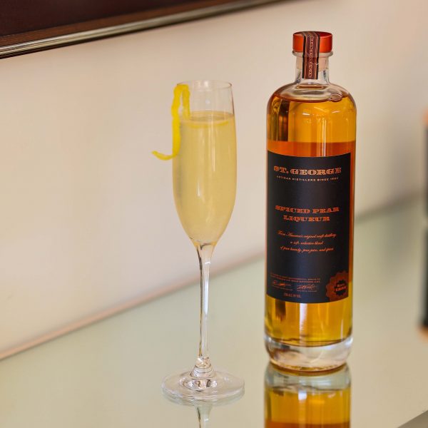 A champagne flute with a lemon twist and a bottle of spiced pear