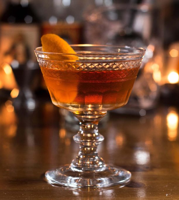 A cocktail in a vintage coupe glass with an orange peel garnich