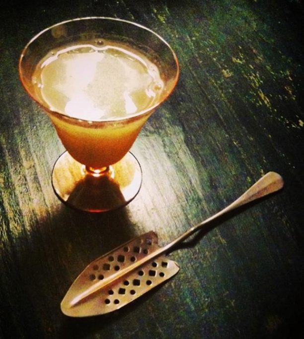 An absinthe spoon on a green countertop