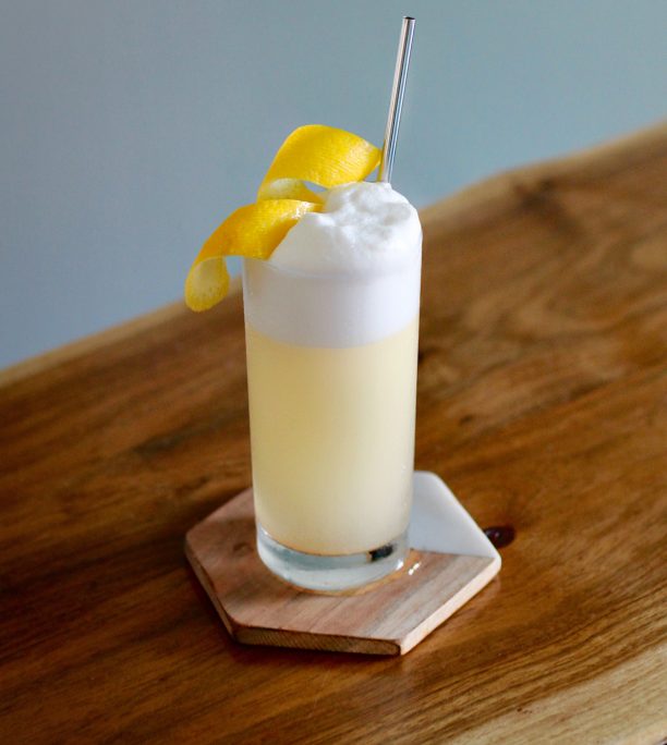 Foamy-topped lemony cocktail ina  highball glass
