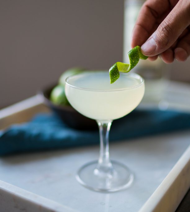 A hand placing a lime twist into a martini